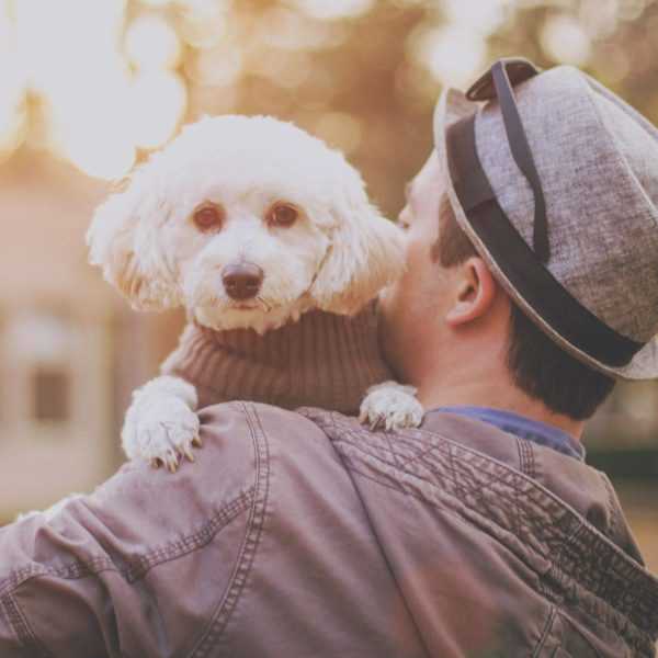 A photograph of a man holding a white dog in his arms.