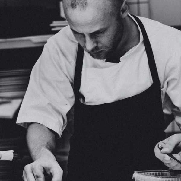 A black and white photo of a chef plating a dish in the kitchen of a restaurant.