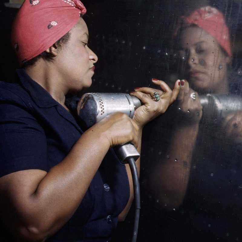 A woman holding a power drill and drilling into a sheet of metal.