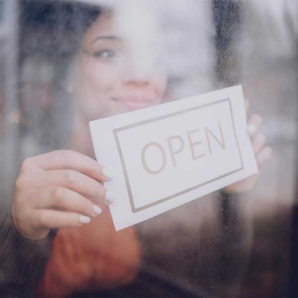 A woman placing a sign in a store window that says Open.