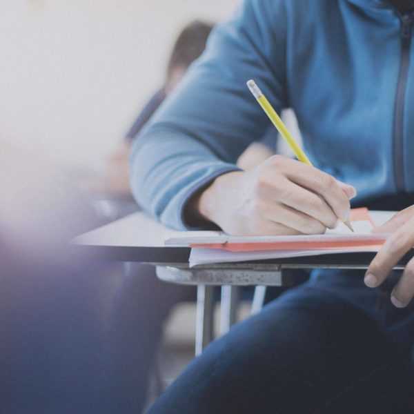 A person sitting in a classroom desk writing with pencil on paper.